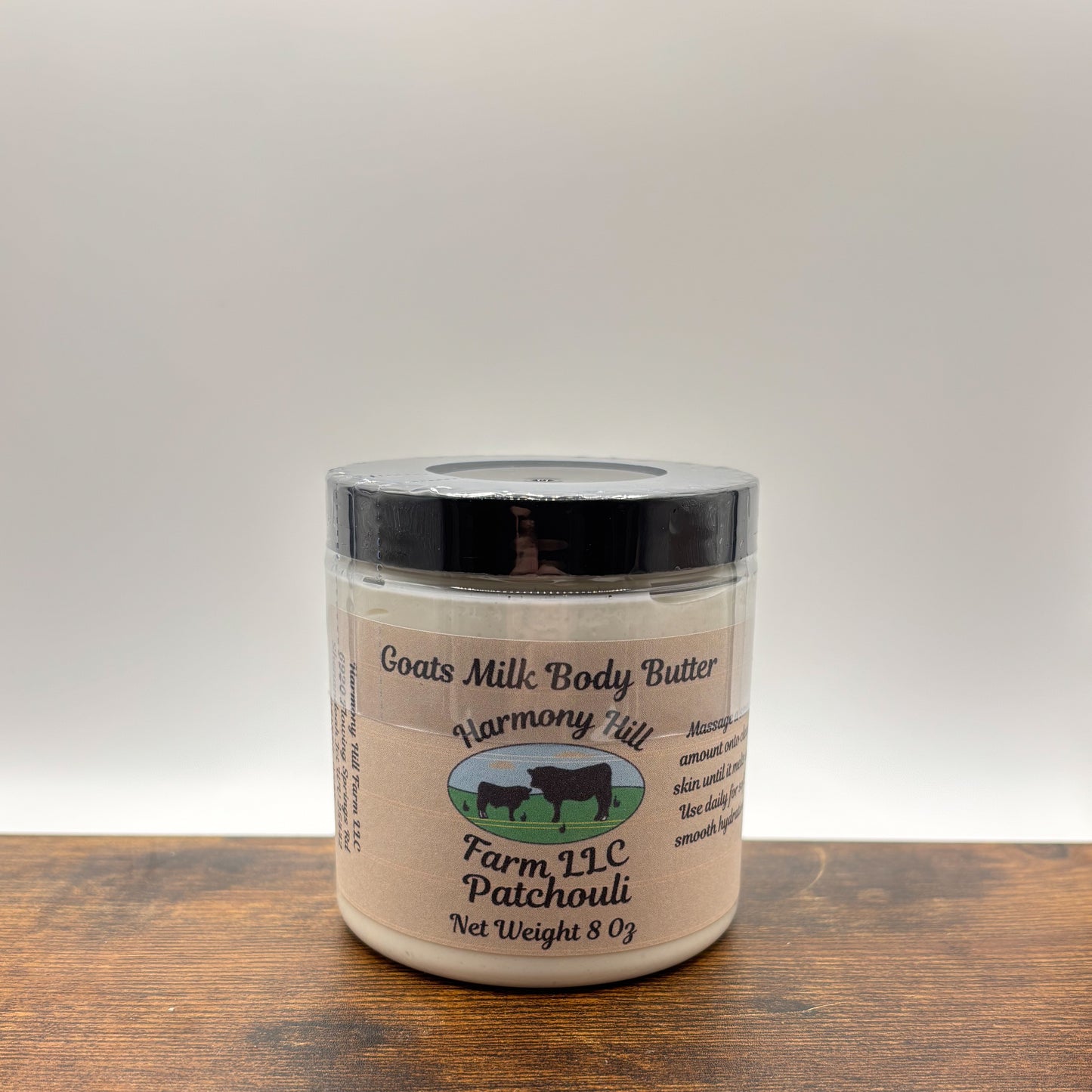 Jar of patchouli goats milk body butter on a wooden surface with a white background
