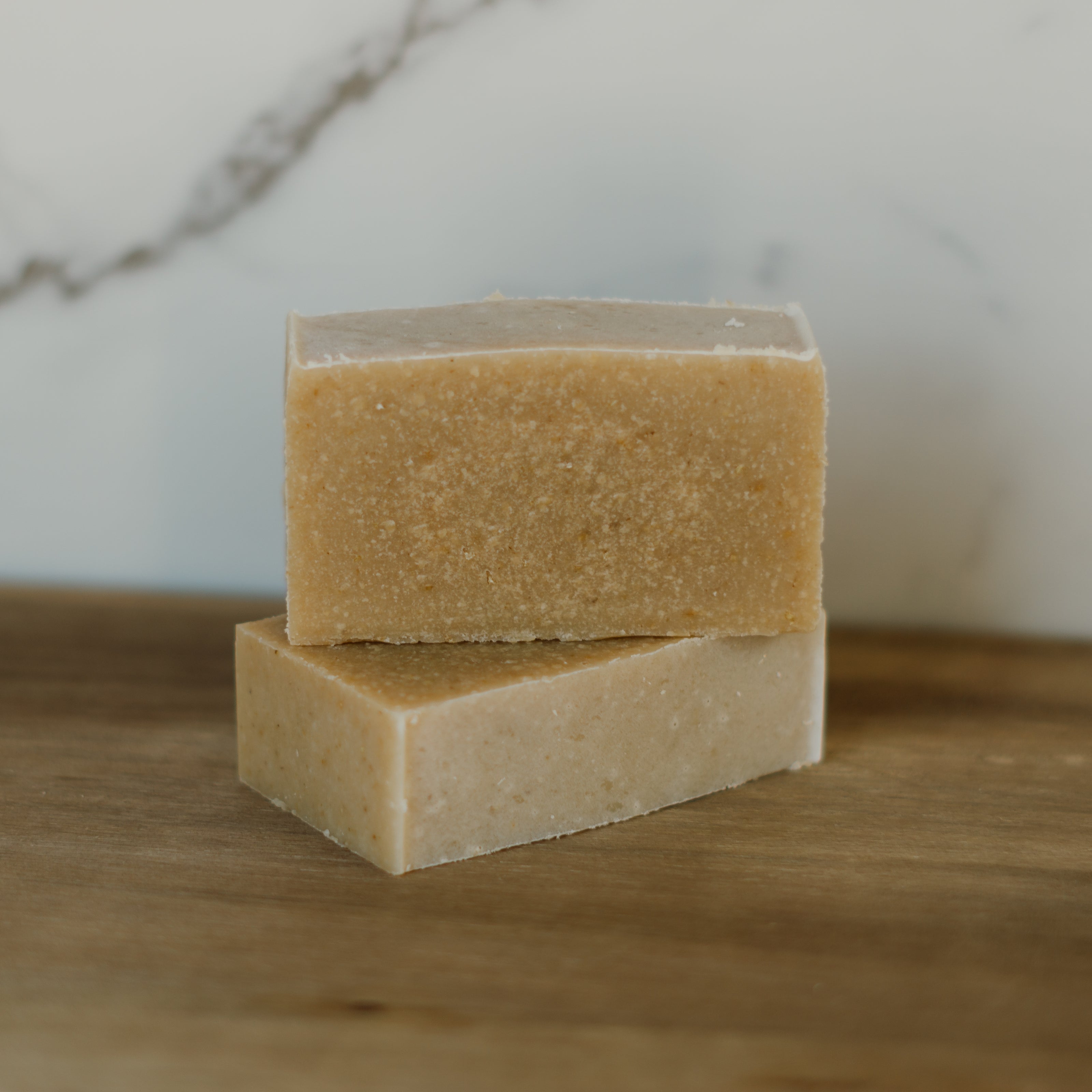 Two bars of soap stacked on a wooden surface with a marble background