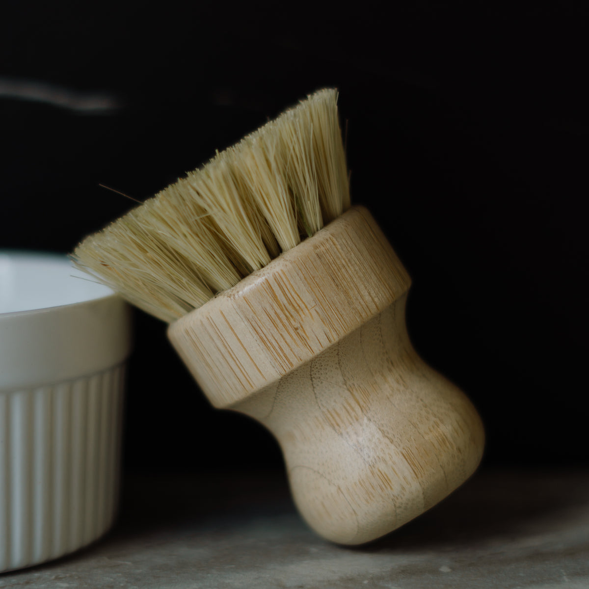 Wooden brush with bristles next to a white container on a dark background