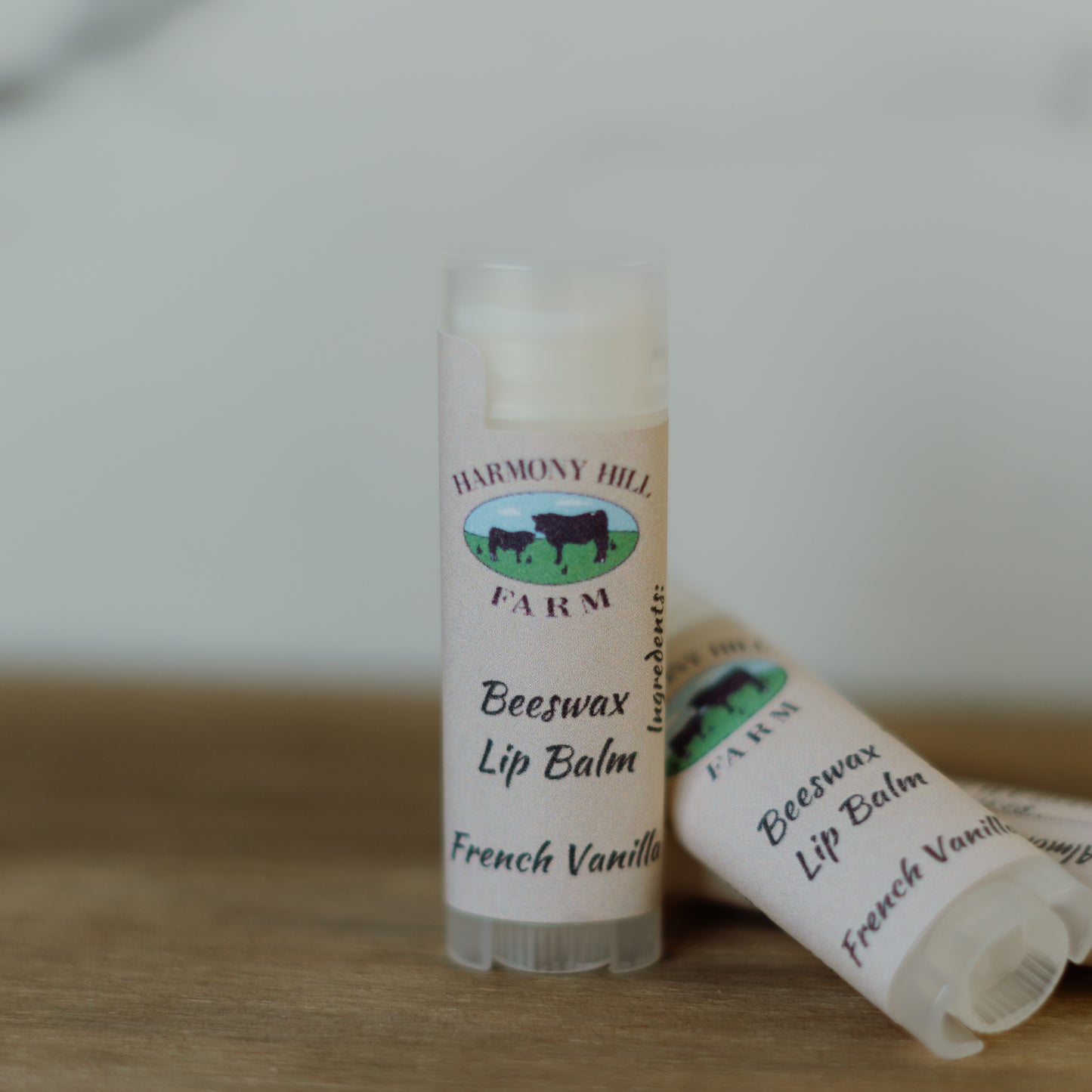 Two lip balms labeled 'Harmony Hill Farm Beeswax Lip Balm French Vanilla' on a wooden surface.