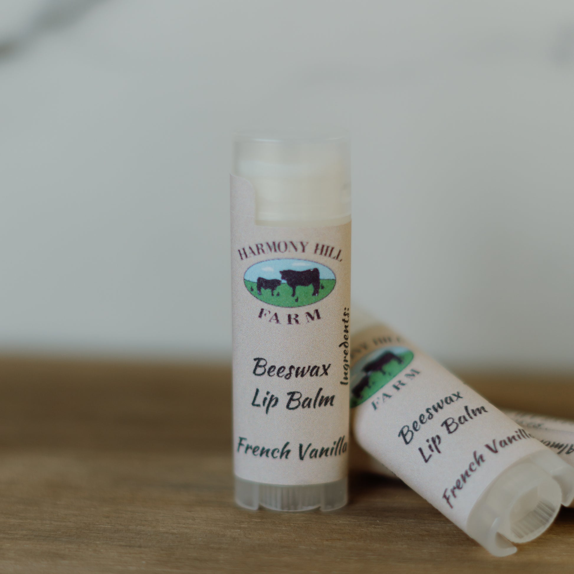 Two lip balms labeled 'Harmony Hill Farm Beeswax Lip Balm French Vanilla' on a wooden surface.