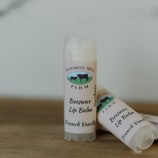 Two lip balms labeled 'Harmony Hill Farm Beeswax Lip Balm French Vanilla' on a wooden surface.