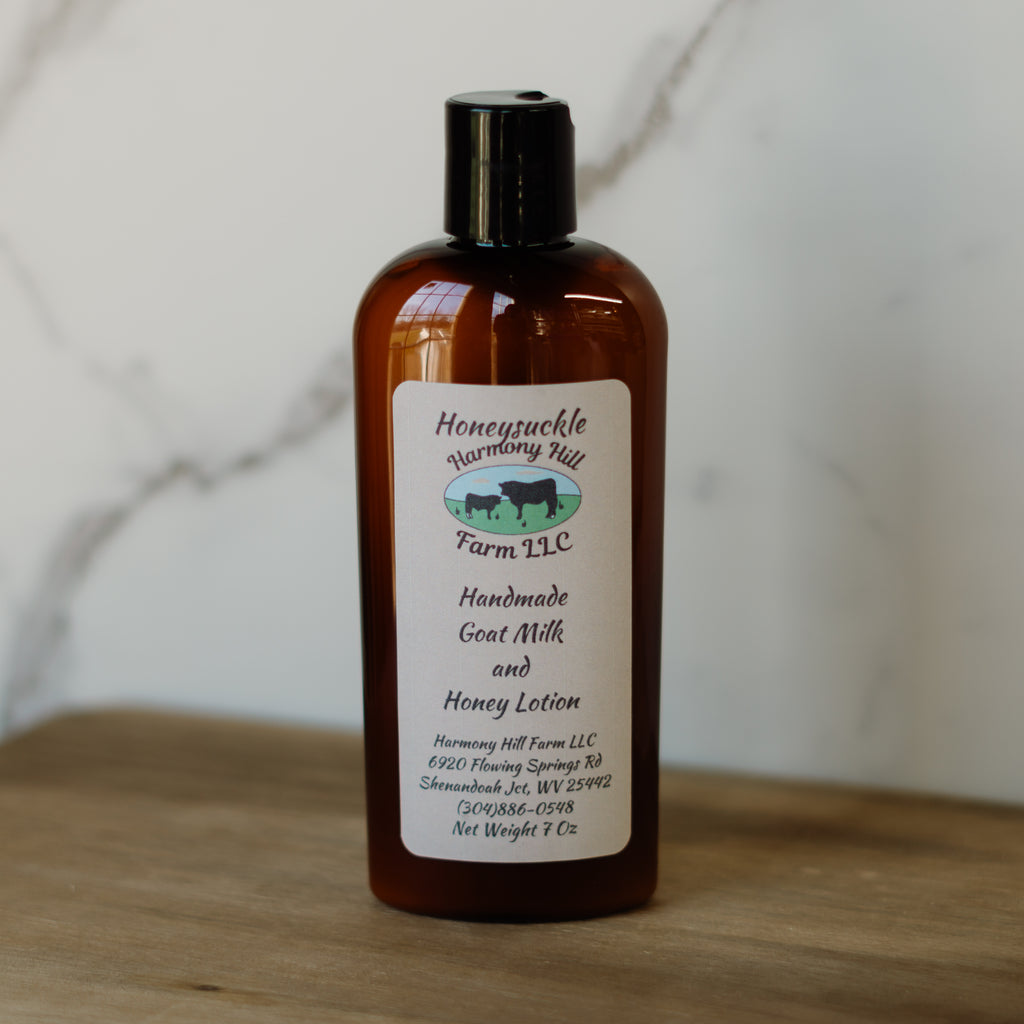 Bottle of Honeysuckle Farm LLC handmade goat milk and honey lotion on a wooden surface with a marble background.