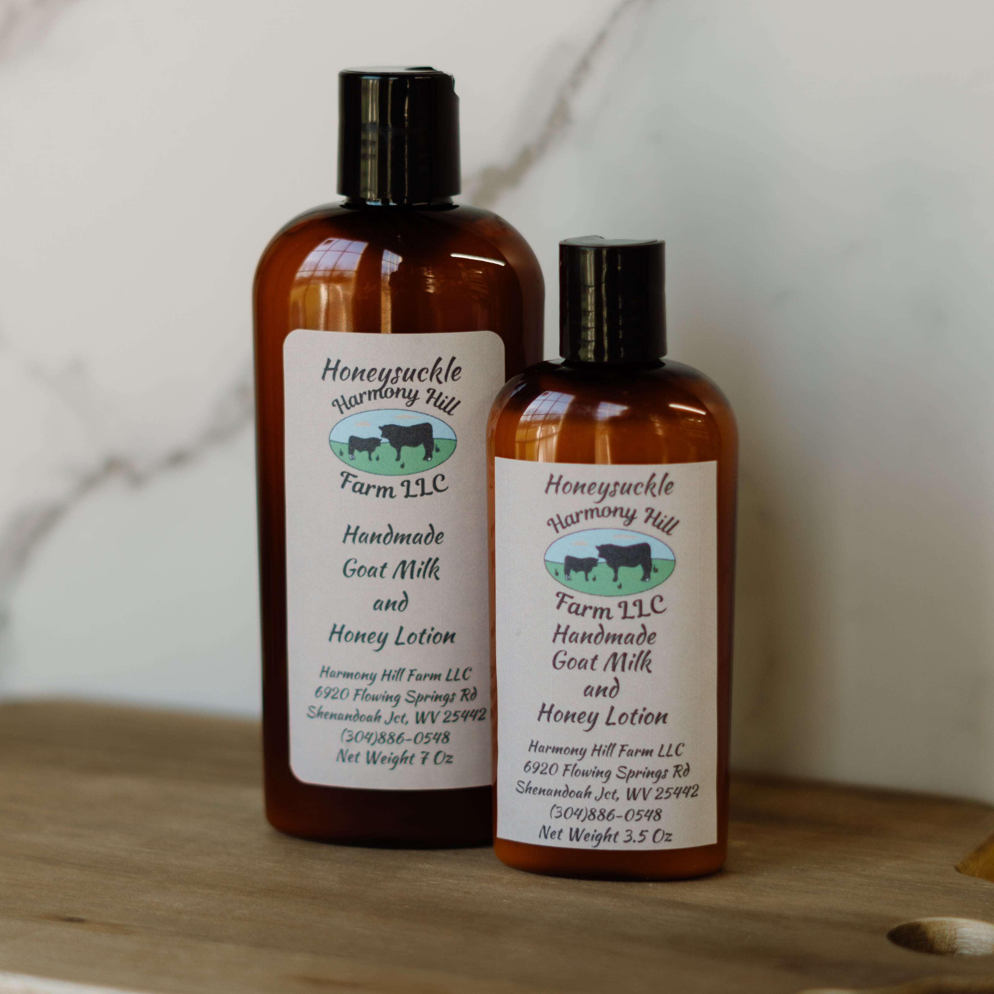 Two bottles of Honeysuckle Harmony Hill Farm LLC handmade goat milk and honey lotion on a wooden surface.