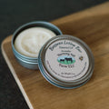 Lavender beeswax lotion bar in a tin with 'Harmony Hill Farm LLC' label on a wooden surface.