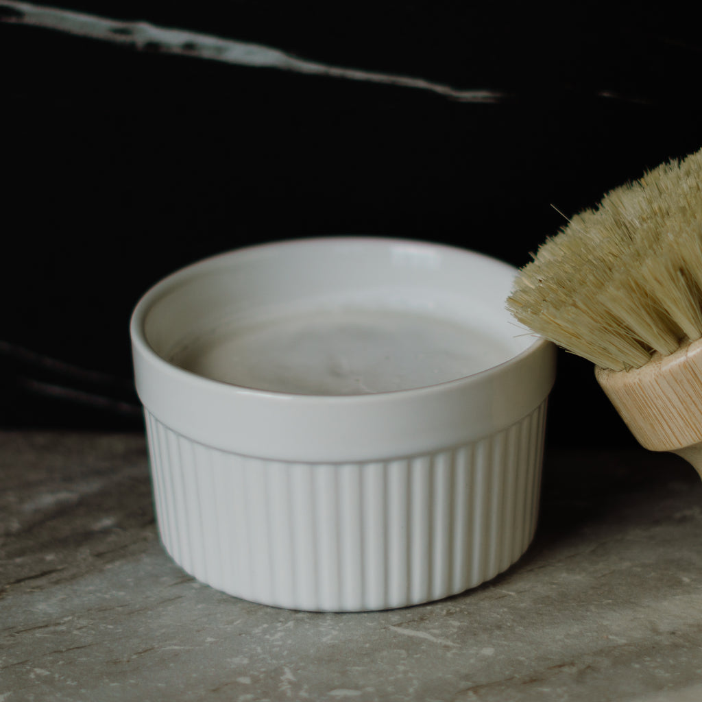 White ceramic bowl with a solid dish soap and wooden brush on a dark surface