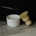 White ceramic bowl with a solid dish soap and wooden brush on a dark surface