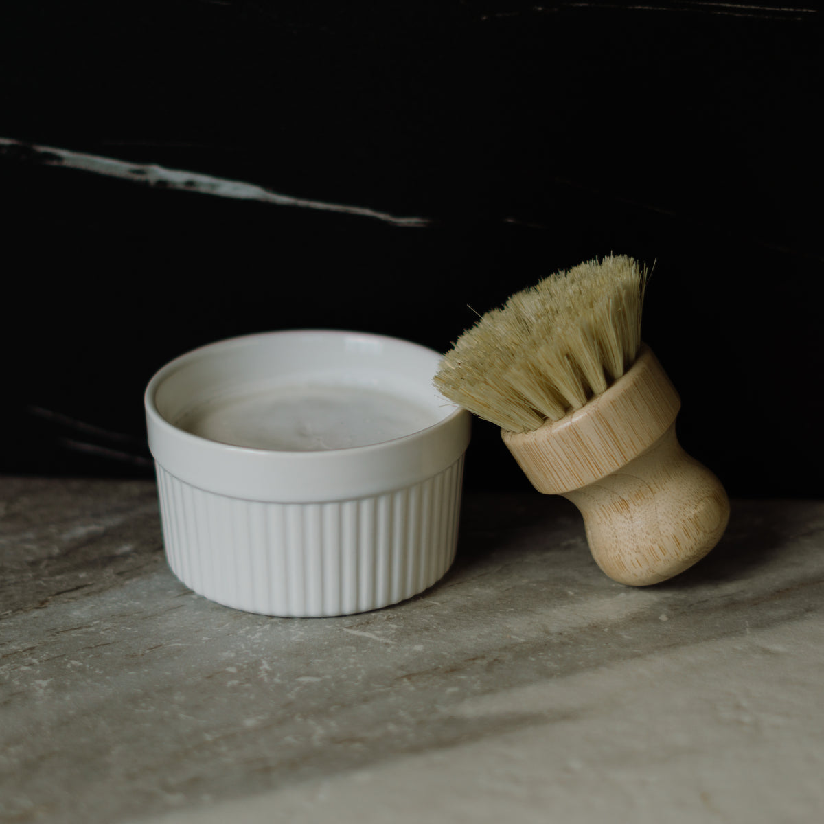 White ceramic bowl with a solid dish soap and wooden brush on a dark surface
