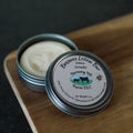 Beeswax lotion bar in a metal tin with 'Harmony Hill Farm LLC' label on a wooden surface.